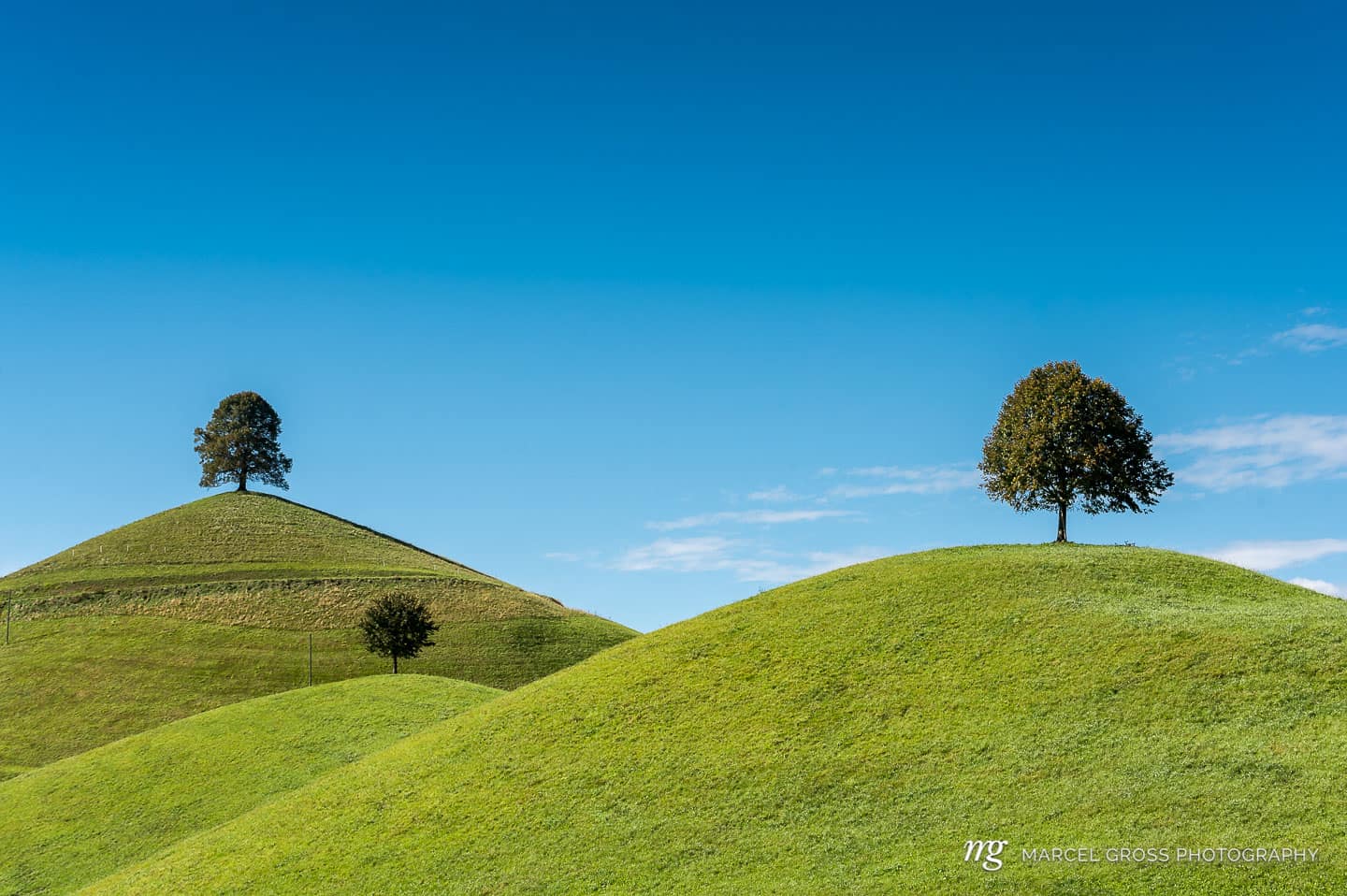 green hills with trees on top against blue sky. Taken by Marcel Gross Photography