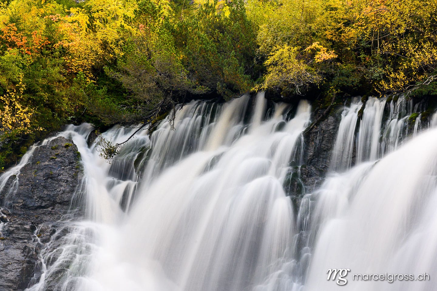 Herbstwasserfall. Sibe Brünne Waterfalls in Lenk in autumn foliage. Marcel Gross Photography