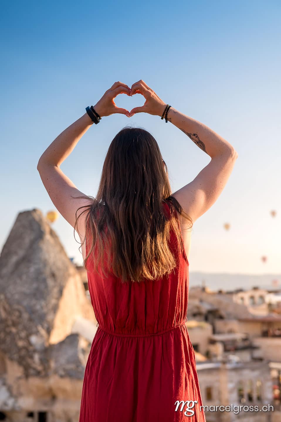 kappadokien bilder. girl in red dress forming a heart with hands. Marcel Gross Photography
