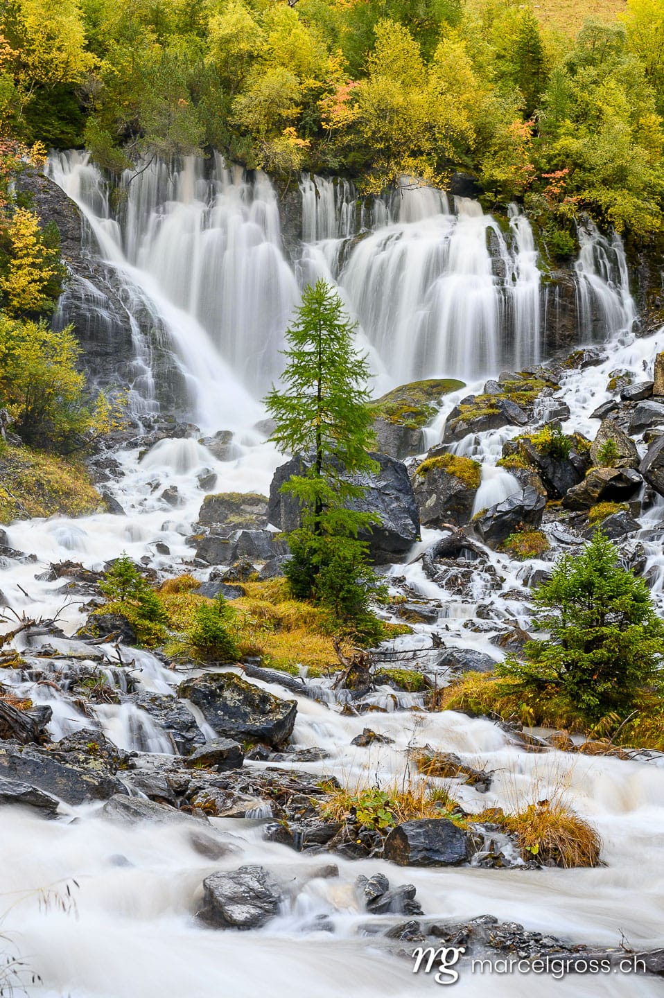 Herbstwasserfall. Sibe Brünne Waterfalls in Lenk in autumn foliage. Marcel Gross Photography